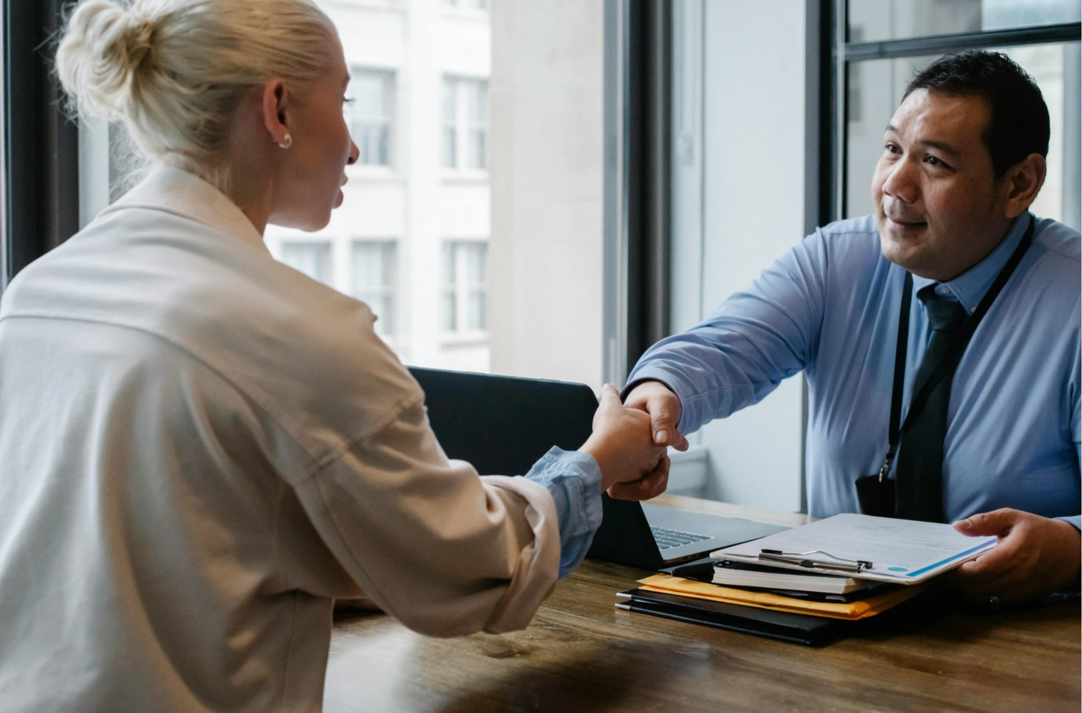 A professional handshake between a woman and a man in an office setting, representing trust and collaboration during an immigration consultation.