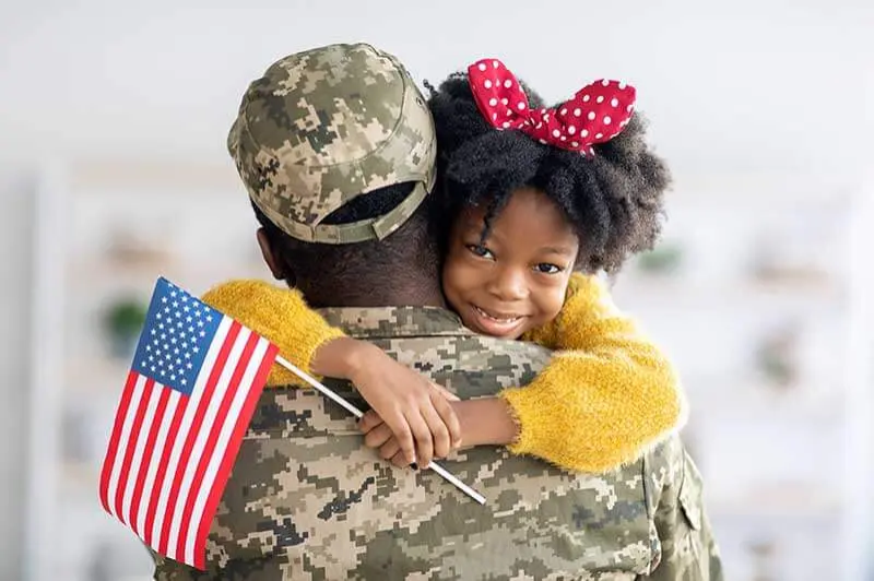 Smiling child hugging a U.S. military parent, holding a small American flag.